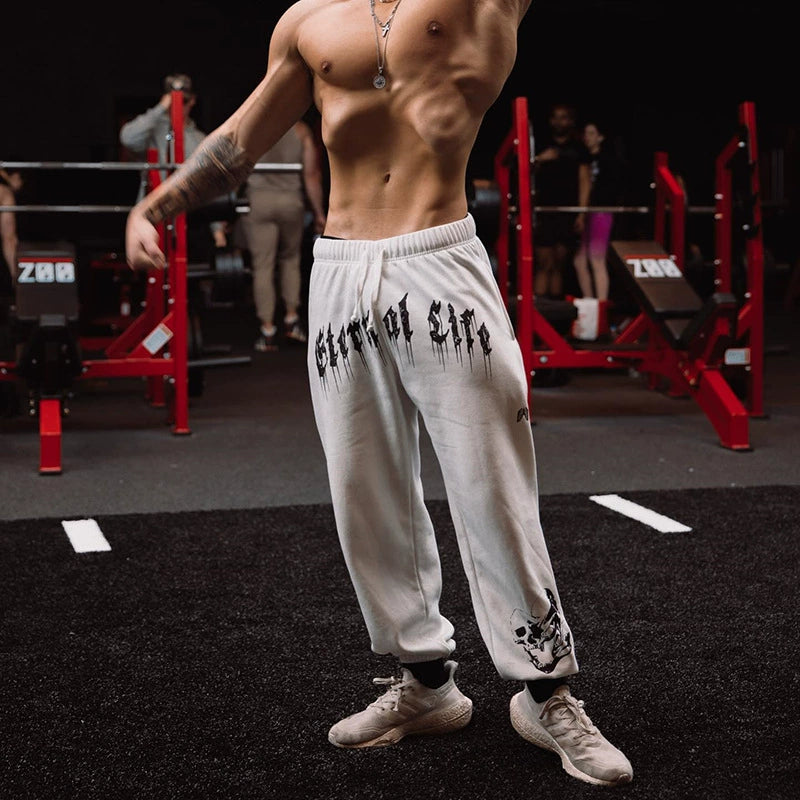 Pantalones deportivos holgados con estampado de calaveras oscuras y tobillos atados para entrenamiento muscular.